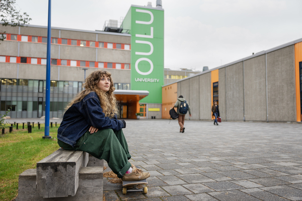 decorative; the main entrance of the University of Oulu Linnammaa campus showing also in the foreground a young person with sitting on a bench with a skateboard